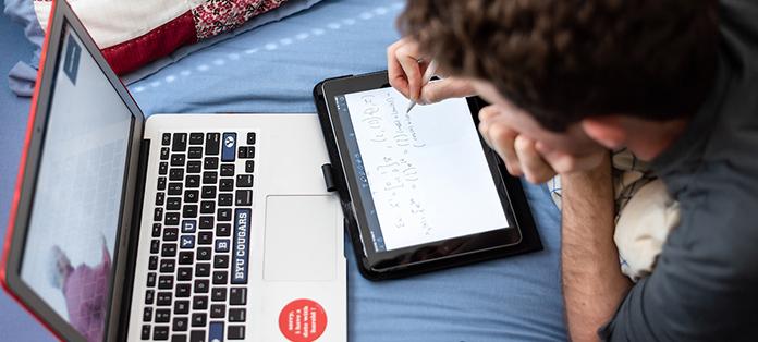 student writes on tablet while watching a lecture on laptop